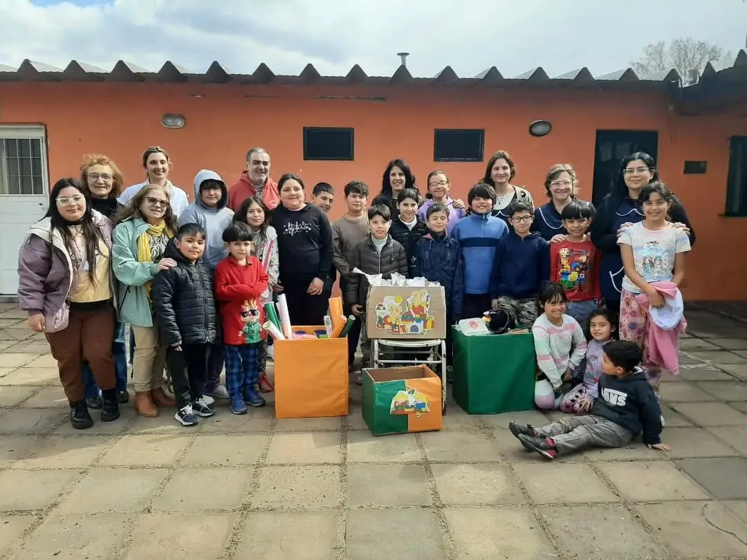 Grupo grande de chicas, chicos y adultos de FUPIS posando en el patio de una escuela junto a cajas de materiales