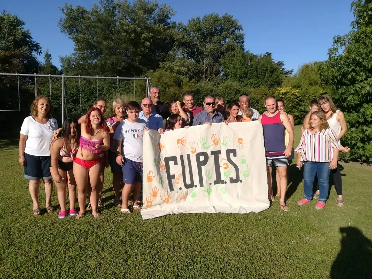 Familias de FUPIS reunidas al aire libre sosteniendo una bandera pintada a mano con manos de colores y la palabra FUPIS